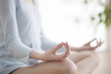 Woman meditating with crossed legs, hands are facing upwards resting on her knees.