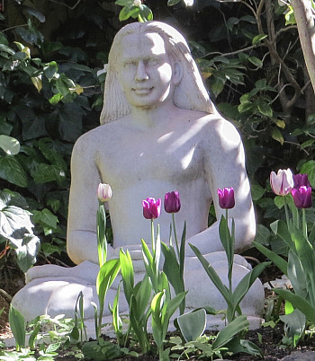 white Babaji statue with purple and white tulips in front