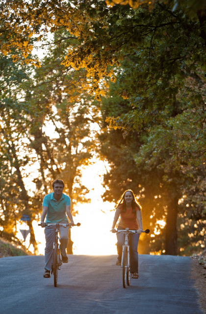Smiling couple riding their bicycle in the forest, trees are covered in golden light during sunset.